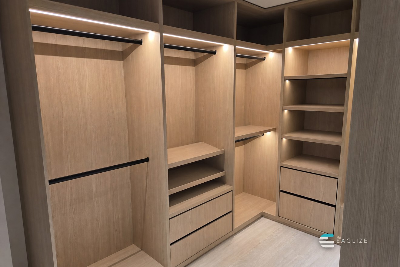 Walk-in wardrobe with open timber carcasses, lit hanging rails, drawer banks and a corner shelf run